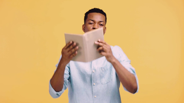 verveelde Afrikaan amerikaanse man met boek boven hoofd geïsoleerd op geel - Video