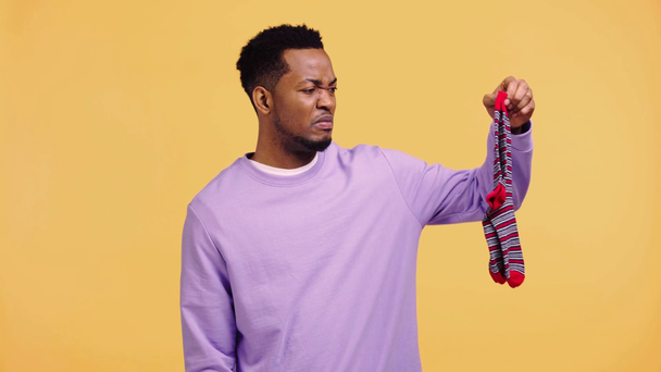 african american man sniffing stinky socks isolated on yellow - Metraje, vídeo