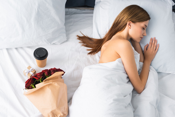 Вид сверху женщины, спящей в постели рядом с бумажной чашкой и букетом
 - Фото, изображение