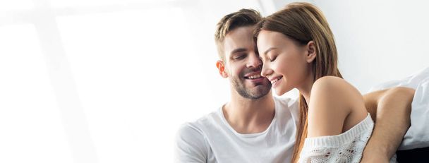panoramic shot of handsome man hugging smiling woman in apartment  - Фото, изображение