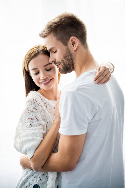 handsome man hugging attractive and smiling woman in apartment  - Photo, Image
