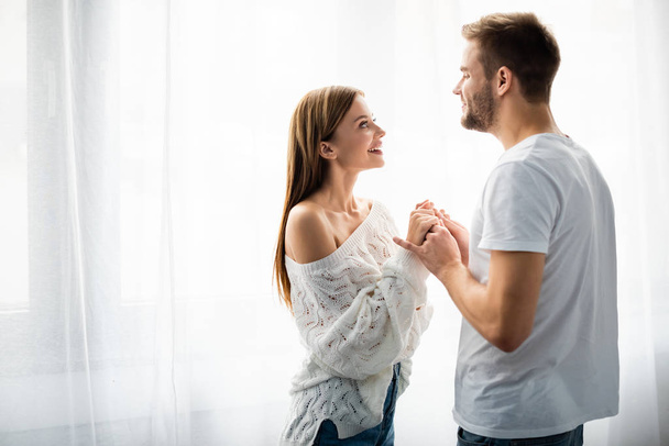 side view of handsome man holding hands with smiling woman in apartment  - Photo, Image