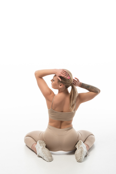 vista trasera de la rubia twerk bailarina en leggings beige sentado en el suelo aislado en blanco
 - Foto, Imagen