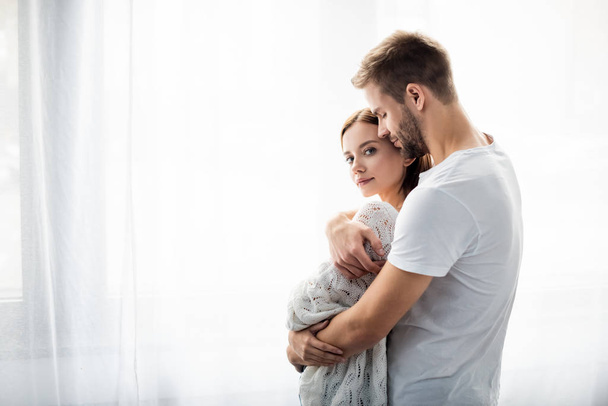 handsome man hugging attractive woman in apartment  - Фото, зображення