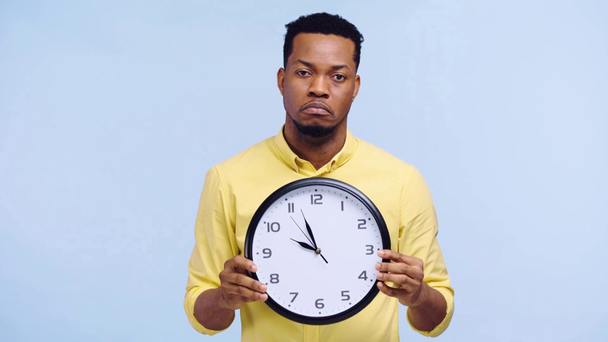 hombre afroamericano molesto sosteniendo reloj aislado en azul
 - Metraje, vídeo