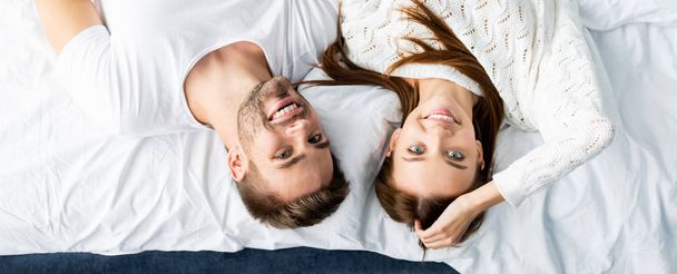 panoramic shot of handsome man and smiling woman looking at camera in apartment - Photo, Image