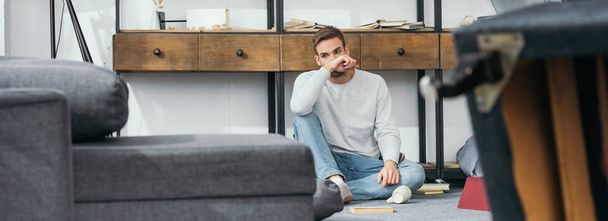 panoramic shot of handsome man sitting in robbed apartment  - Fotografie, Obrázek