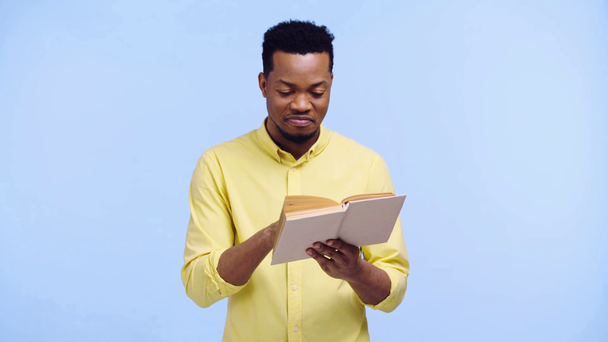 χαμογελαστός Αφροαμερικάνος διαβάζοντας βιβλίο απομονωμένο στο μπλε - Πλάνα, βίντεο
