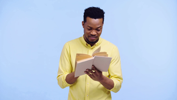 uśmiechnięty Afrykanin Amerykanin czyta książkę odizolowany na niebiesko - Materiał filmowy, wideo