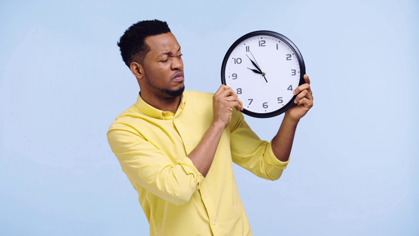 sad african american man looking at clock isolated on blue - Кадри, відео