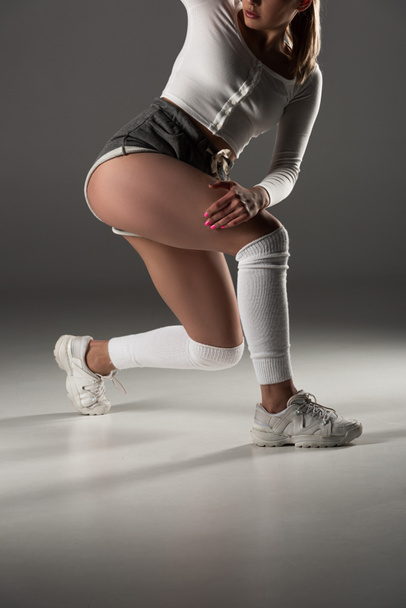 cropped view of young sexy girl in shorts twerking on grey background - Foto, afbeelding