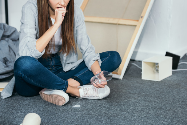 cropped view of sad woman sitting on floor in robbed apartment  - Фото, изображение