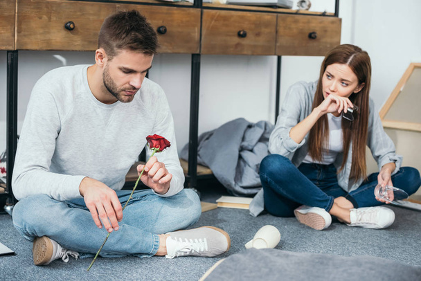 sad woman and handsome man sitting on floor in robbed apartment  - Foto, afbeelding
