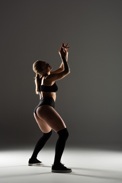 oldal kilátás szexi lány fekete ruhában twerking árnyékban szürke háttér - Fotó, kép