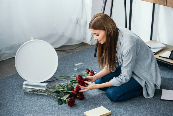 attractive and sad woman holding flowers in robbed apartment  - Φωτογραφία, εικόνα