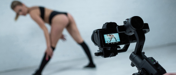 selective focus of cameraman shooting sexy blonde girl in black outfit twerking near white brick wall - Photo, Image
