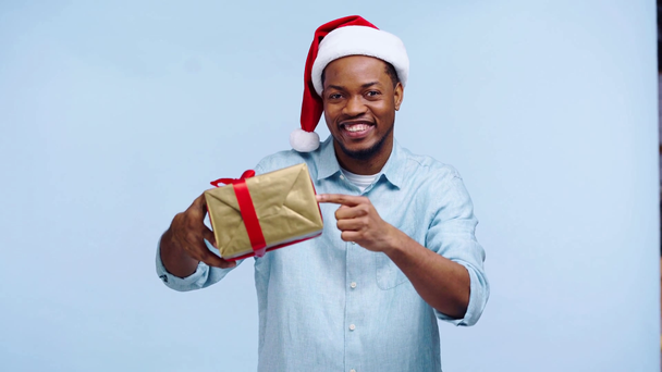 Mutlu Afro-Amerikan adam mavi üzerinde kapalı bir hediye kutusu gösteriyor. - Video, Çekim