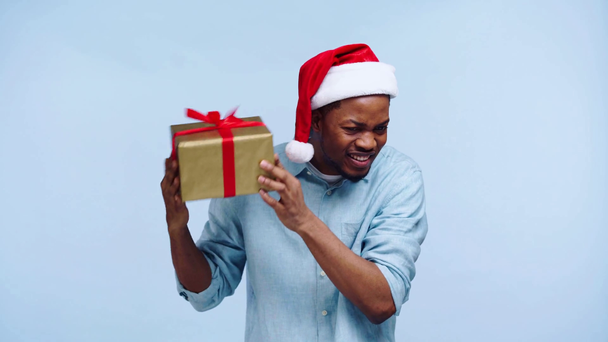 Любопытный африканский американец трясет подарочную коробку, изолированную на голубом
 - Кадры, видео