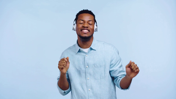 Αφροαμερικάνος με ακουστικά που χορεύει απομονωμένος στο μπλε - Πλάνα, βίντεο