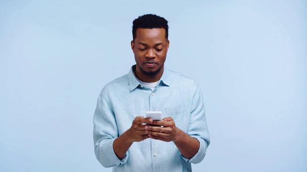 Αφροαμερικάνος συνομιλεί σε smartphone απομονωμένο σε μπλε - Πλάνα, βίντεο
