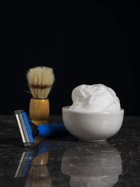 Shaving brush, foam and a man's razor on a stone table on a black background. - 写真・画像