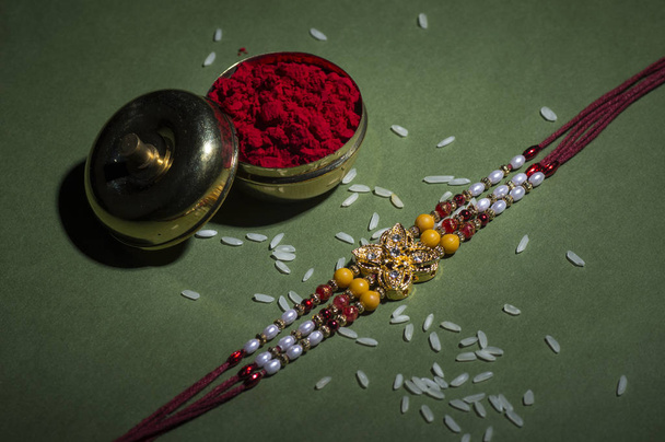 Indian festival: Raksha Bandhan background with an elegant Rakhi, Rice Grains and Kumkum. A traditional Indian wrist band which is a symbol of love between Brothers and Sisters. - Photo, Image