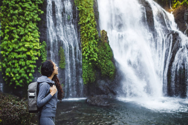 Frau beobachtet Wasserfall banyumala in bali. lange lockige Brünette  - Foto, Bild