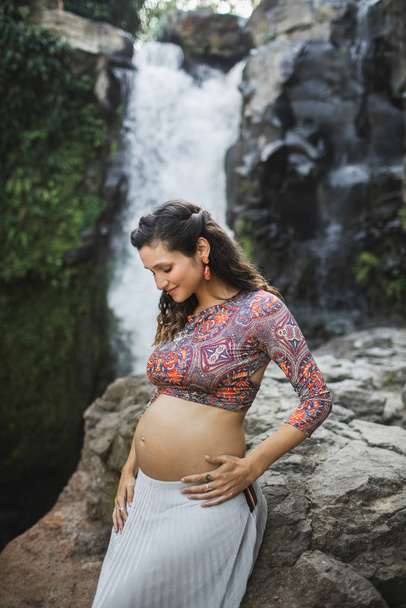 Jovem mulher grávida autêntica perto de cachoeira cascata incrível. N
 - Foto, Imagem
