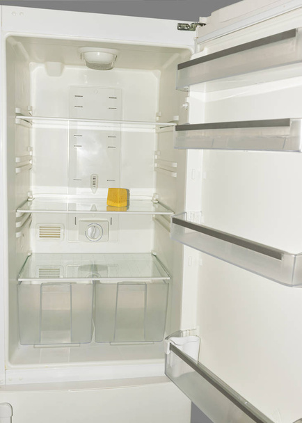 A piece of yellow old cheese lies on the empty shelves of the refrigerator. The concept of diet and hunger. - Photo, Image
