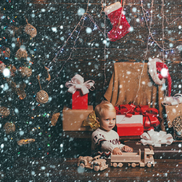 Christmas children. Funny kid holding Christmas gift. Opening gifts on Christmas and New Year. Christmas card. Portrait kid with gift on wooden background. - Zdjęcie, obraz