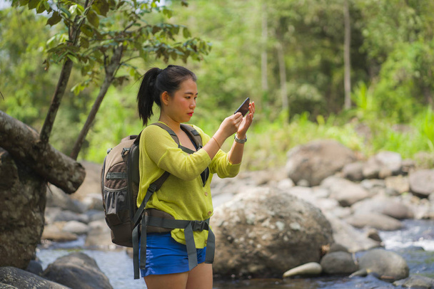 happy Asian Chinese woman carrying backpack trekking on mountains crossing river enjoying holiday nature and fresh environment hiking taking photo with mobile phone - 写真・画像