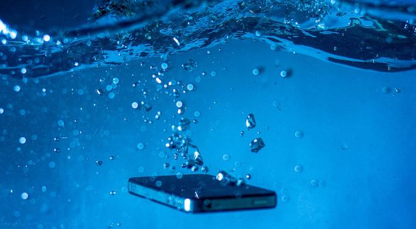 black and white phone dropped into the water. phone in water. blue water. phone in water bubbles.phone sinks in water - 写真・画像