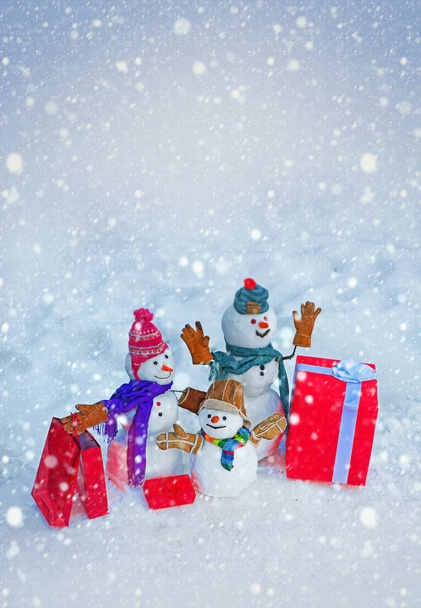 配達ギフトやギフトの感情。幸せな雪だるまの家族雪だるまは冬の帽子と赤い鼻のスカーフで立っています。贈り物の袋を持つ雪だるま. - 写真・画像
