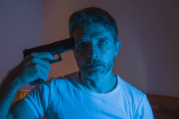 dramatic portrait in cinematic edgy lighting of young desperate and sick man pointing gun to his head for committing suicide shooting himself sitting on bed at night in horror  - Fotoğraf, Görsel