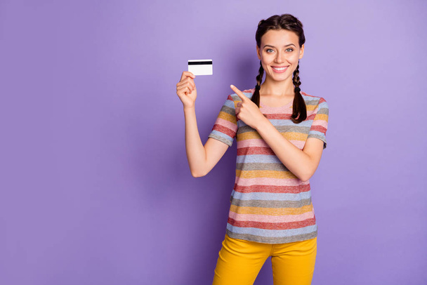 Photo of pretty lady holding credit card online shopping advising best way for lazy people direct finger wear casual t-shirt yellow pants isolated pastel purple color background - Фото, изображение