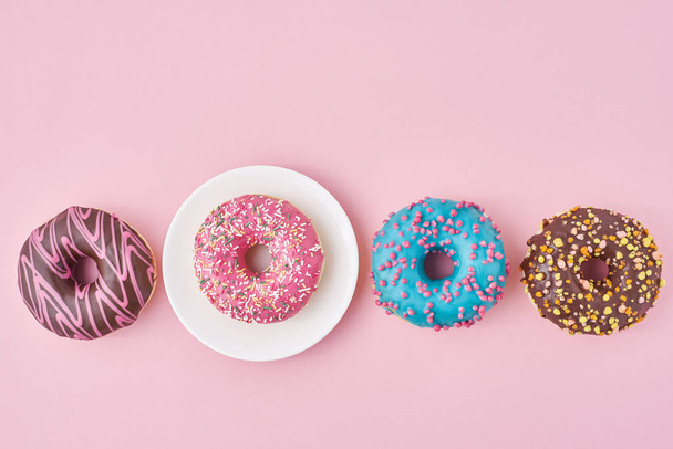 Different colorful donuts and plate on the pink background. Creative food concept - Photo, Image