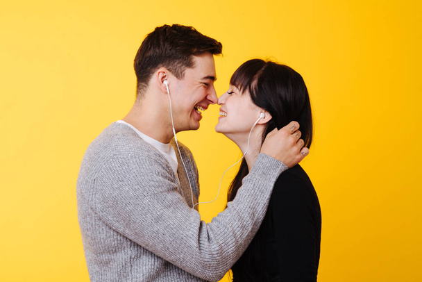 Happy couple in love kissing while listening to the musicover over yellow - 写真・画像