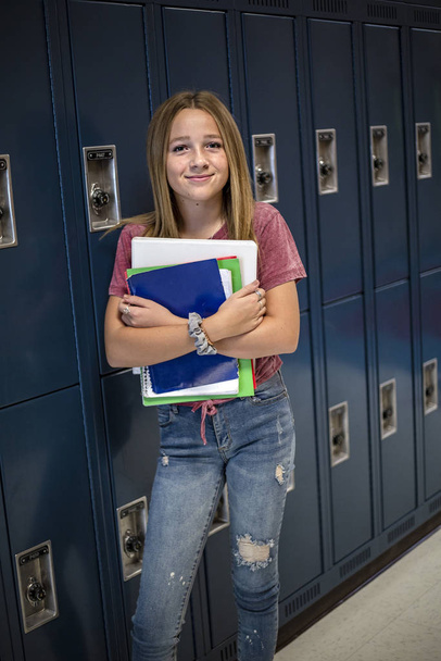 Portrait of a female Junior High school Student standing in a school hallway. Smiling school girl looking and holding her books during breaks in the day - Photo, Image