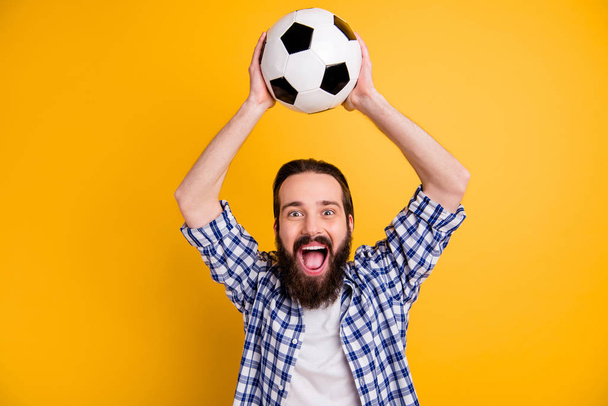 Portrait of his he nice attractive cheerful cheery overjoyed bearded guy fan in checked shirt holding in hands over head throwing ball isolated over bright vivid shine vibrant yellow color background - Foto, Imagem