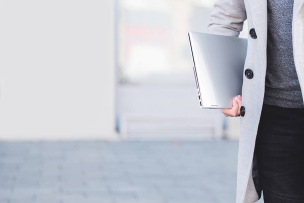 Cropped image of modern dressed businessman  carrying laptop. The concept of a busy life today full of technology. Picture with copy space - Zdjęcie, obraz