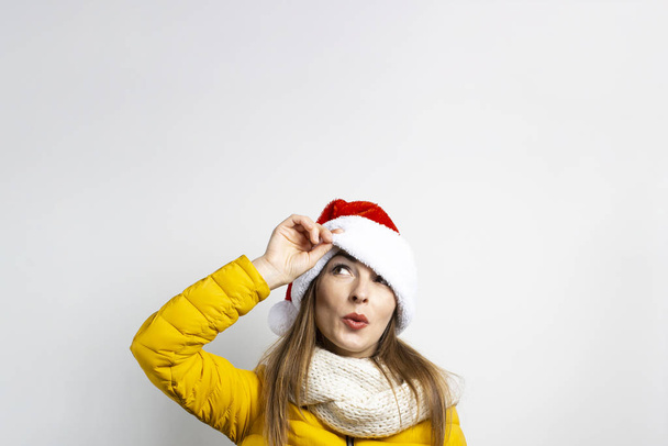 Молода жінка дивиться з-під капелюхів Санта-Клауса на світлому тлі. Концепція зими, зимові канікули, Різдво, Новий рік. Смішний настрій, емоції, сюрприз, шок - Фото, зображення