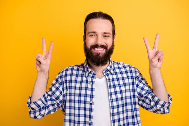 Close-up portrait of his he nice attractive cheerful cheery funky brunette bearded guy in checked shirt showing double v-sign isolated on bright vivid shine vibrant yellow color background - Fotó, kép