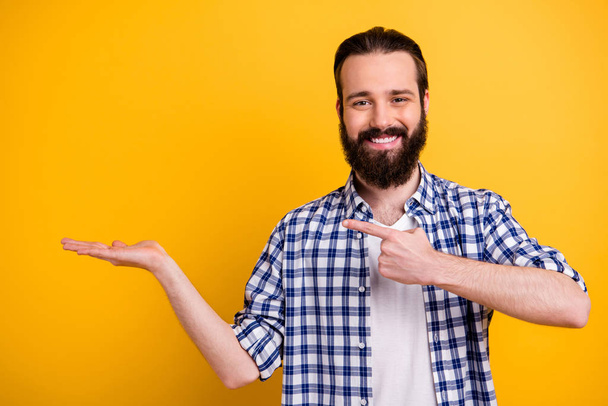 Portrait of nice attractive cheerful cheery confident content bearded guy in checked shirt showing holding invisible object on palm isolated over bright vivid shine vibrant yellow color background - Foto, Imagen