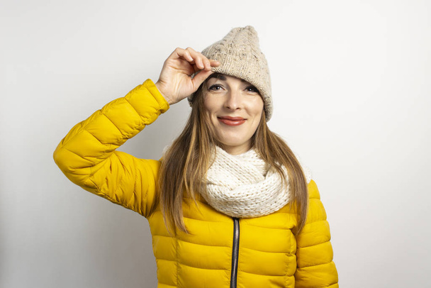 Young woman peeks out from under a hat on a light background. Winter concept, winter fashion, winter clothes. Funny mood, emotions - Foto, afbeelding