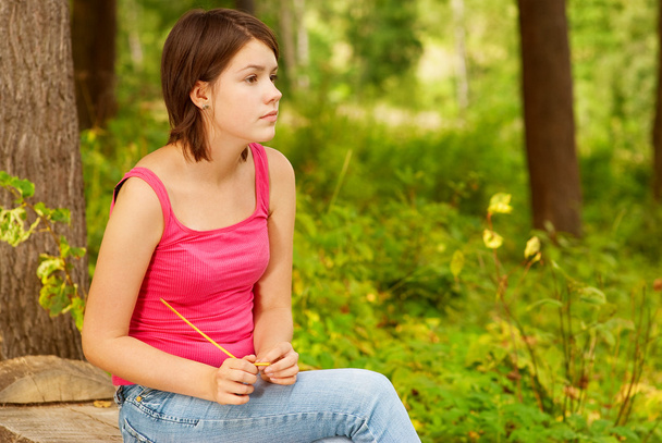 Дівчина на відкритому повітрі в лісі сидить на колоді
 - Фото, зображення