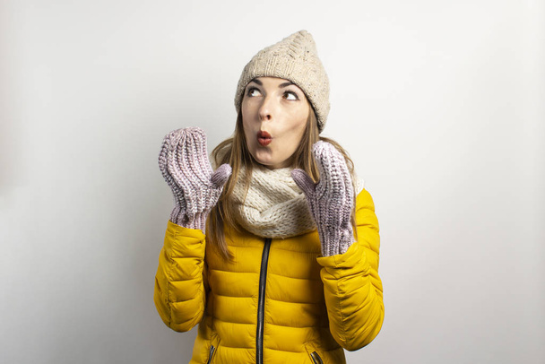 Young woman in a hat and mittens caps on a light background. Winter concept, winter fashion, winter clothes. Funny mood, emotions, surprise, shock - Фото, изображение