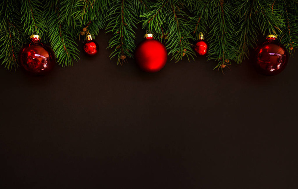 Christmas card concept with fir tree branches and red shiny balls on dark background - text space. Merry Christmas and Happy Holidays greeting card. Flat lay, top view. Copy space for your text. - Foto, Bild