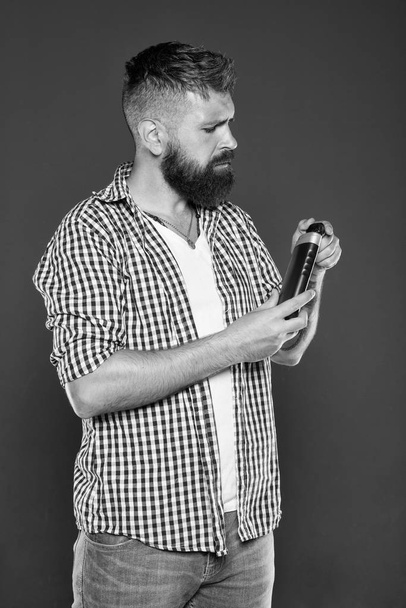 The best shampoo for his hair. Bearded man holding shampoo bottle on grey background. Hipster with beard and mustache choosing shampoo for cleaning hair. Daily strengthening shampoo for men - 写真・画像