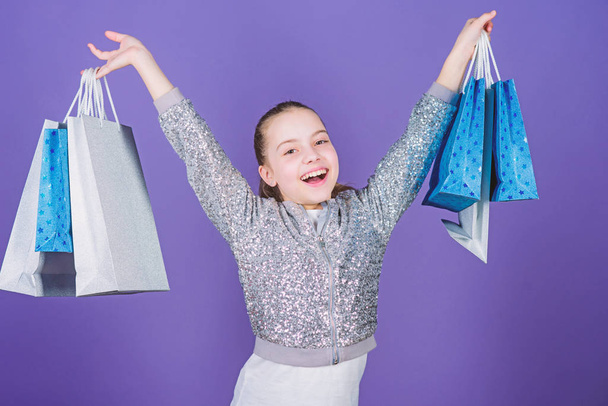 Get better looking. Black friday. Sale discount. Shopping day. Child hold bunch packages. Kids fashion. Birthday girl. Surprise gift. Girl with shopping bags violet background. Shopping and purchase - Фото, изображение