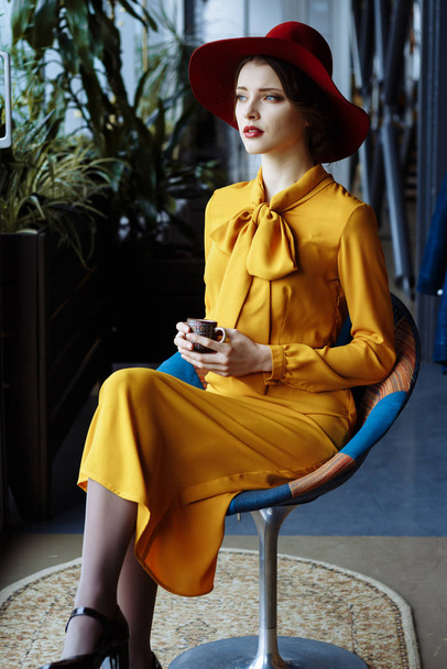 Mädchen in einem Café mit einer Tasse Kaffee und einem Hut. Porträt eines sinnlichen jungen Mädchens mit Schlapphut und Bluse mit Schleife. Schöne brünette Frau im Café mit einer Tasse Kaffee - Foto, Bild